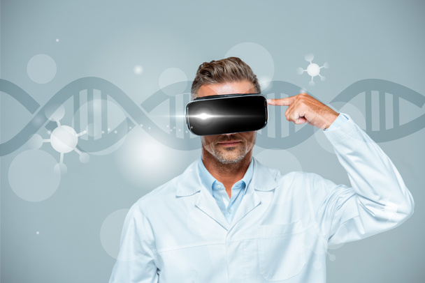 scientist  in virtual reality headset pointing on his head isolated on grey with dna, artificial intelligence concept - Photo, Image