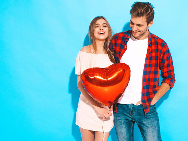 Portrait of Smiling Beautiful Girl and her Handsome Boyfriend holding  heart shaped air balloons and laughing. Happy  Family. Love. Happy Valentine's Day. Posing near blue wall - Фото, изображение