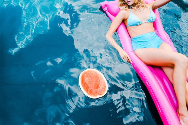 cropped view of girl in swimsuit resting on pink inflatable mattress in swimming pool with watermelon - 写真・画像