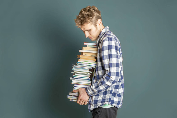 Gelegenheitsstudentin trägt riesigen Stapel Bücher auf dunklem Hintergrund - Foto, Bild