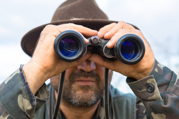 Un cazador en un sombrero con prismáticos busca presas
 - Foto, imagen