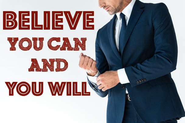 cropped image of businessman buttoning cuff isolated on white with "believe you can and you will" lettering  - Foto, Imagen