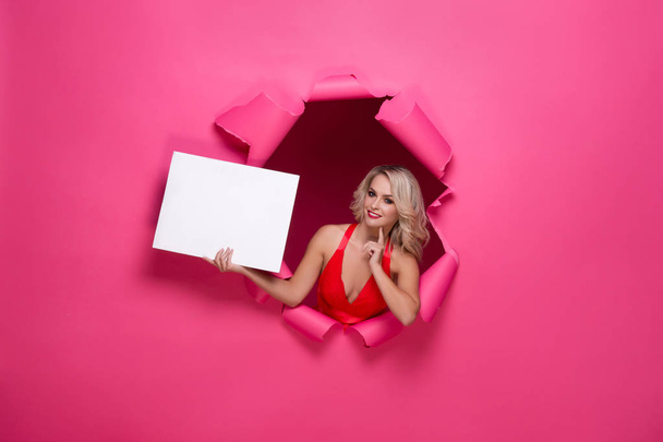 Young and beautiful woman in pink dress holding paper banner over torn paper background. St. Valentines day concept. - Фото, зображення