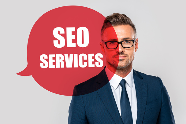 portrait of handsome businessman in suit and glasses looking at camera isolated on grey with seo services - Foto, afbeelding