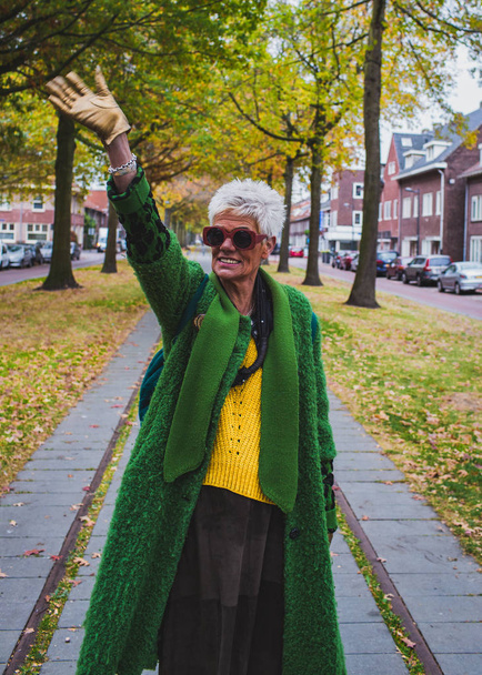 Portrait of a senior friendly woman in green coat walking in the autumn city - Foto, Imagen