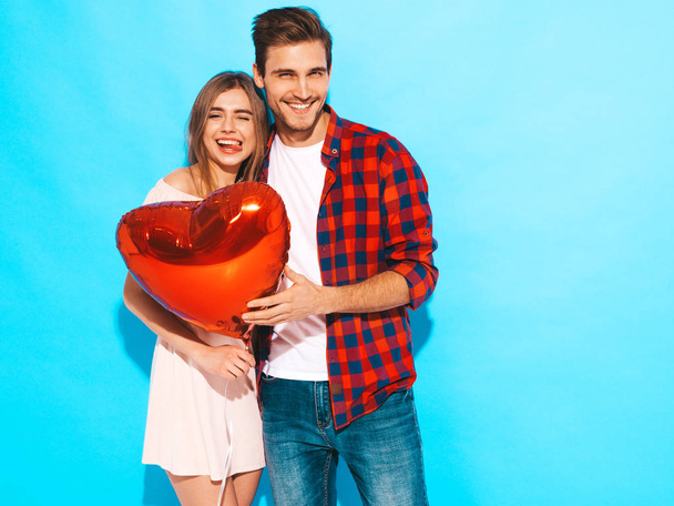 Portrait of Smiling Beautiful Girl and her Handsome Boyfriend holding  heart shaped air balloons and laughing. Happy  Family. Love. Happy Valentine's Day. Posing near blue wall - Zdjęcie, obraz