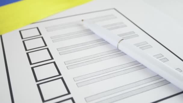 Bolígrafo blanco acostado en papeleta de votación con casilla de verificación de voto y bandera ucraniana. Concepto para el registro de votantes y la participación en elecciones en Ucrania
 - Imágenes, Vídeo