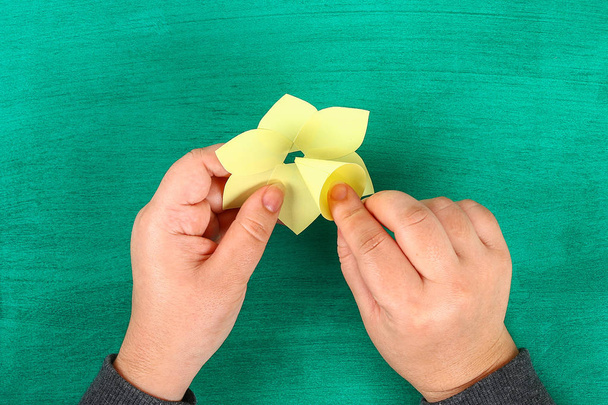 DIY spring flowers daffodils of yellow paper on a green background. Gift ideas, decor for spring, Easter. Handmade. Step by step. The process of crafts. Top view. Childrens Easter crafts. - 写真・画像