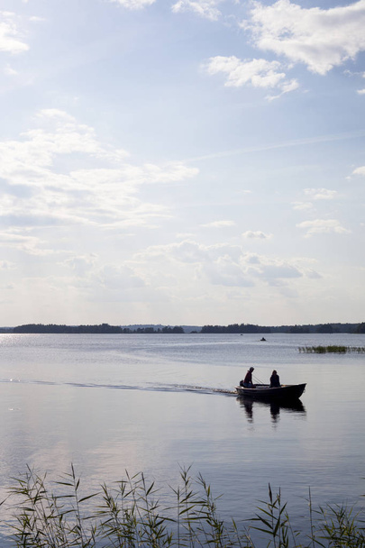 Лодка с двумя людьми, плывущими по озеру на закате с сияющим солнцем - Фото, изображение
