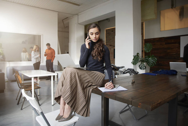 Shot of young businesswoman talking with somebody on her cell phone while sitting at the office and working.  - Foto, Imagen