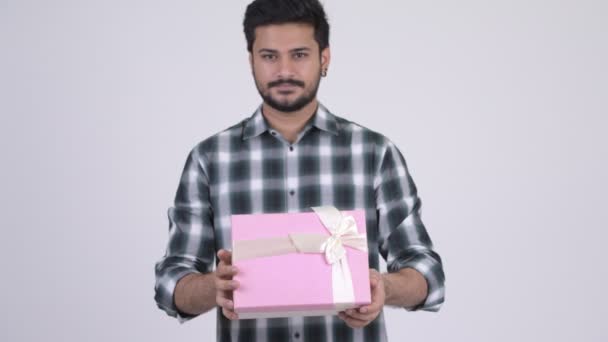 Portrait of young happy bearded Indian man giving gift box - Metraje, vídeo