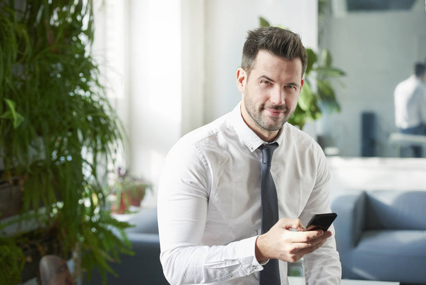 Portrait shot of businessman using his mobile phone and text messaging while sitting in the office.  - Foto, Bild