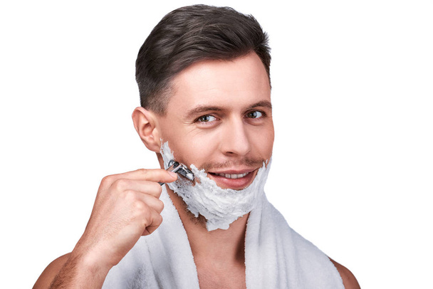 Férfi szépség. Borotválkozás egy borotvával, és mosolyogva, elszigetelt fehér jóképű férfi portréja - Fotó, kép