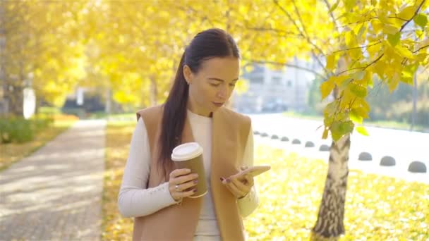 Fall concept - beautiful woman drinking coffee in autumn park under fall foliage - Filmati, video