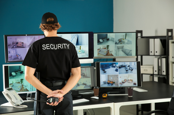 Security guard with portable radio transmitter monitoring modern CCTV cameras in surveillance room - Photo, Image