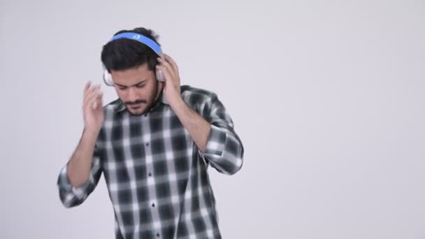 Portrait of young happy bearded Indian man listening to music - Video