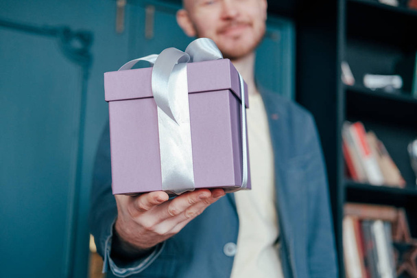 Dárková krabice s šedá stříbrná stuha v rukou mladých attracrive člověka na modrém pozadí - Fotografie, Obrázek