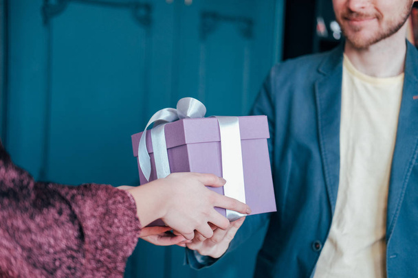 Woman get gift box with gray silver ribbon from young attracrive man on blue background - Foto, Imagem
