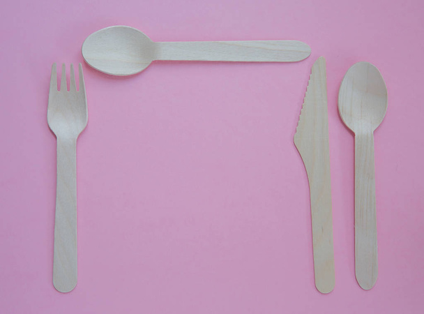 Una disposición plana de cubiertos de madera sostenibles y reciclables que incluye un cuchillo, tenedor y cuchara para la cena en un entorno de lugar y sobre un fondo rosa con espacio para copiar
 - Foto, imagen