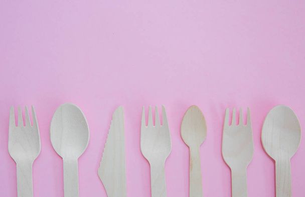 A flat lay of a variety of sustainable and environmentally friendly wooden cutlery including knife, fork and spoon with copy space on a pink background - 写真・画像