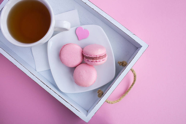Завтрак с розовыми макаронами и чай на белой деревянной дорожке на светло-розовом фоне.
. - Фото, изображение