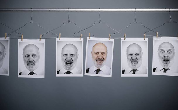 Collection of man's portraits with different facial expressions hanging in line with hangers - 写真・画像