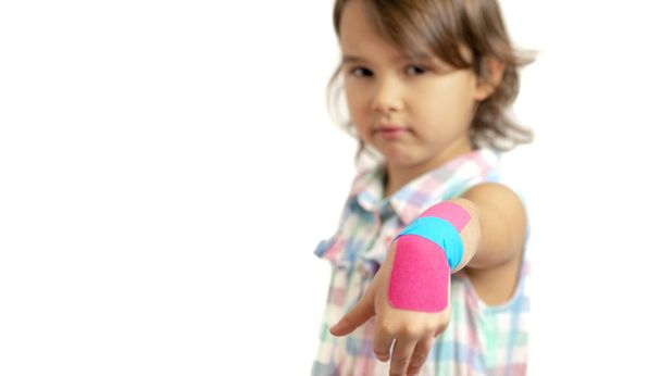 Kleines Mädchen zeigt ihr bandagiertes Handgelenk mit Kinesiobändern - Foto, Bild