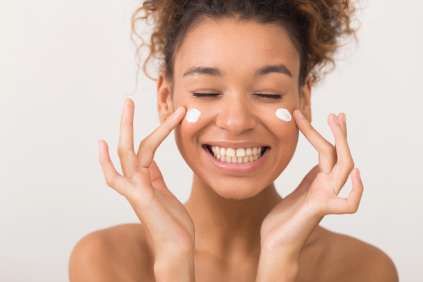 Laughing girl applying moisturizing cream on her face - Zdjęcie, obraz