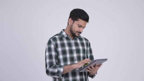 Portrait of young happy bearded Indian man using digital tablet - Filmati, video