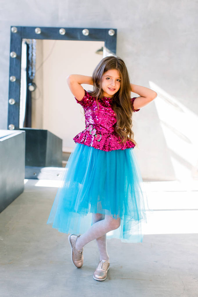 Portrait of little fashion kid girl in a pink shiny blouse and a blue skirt on gray loft background - Foto, Imagem