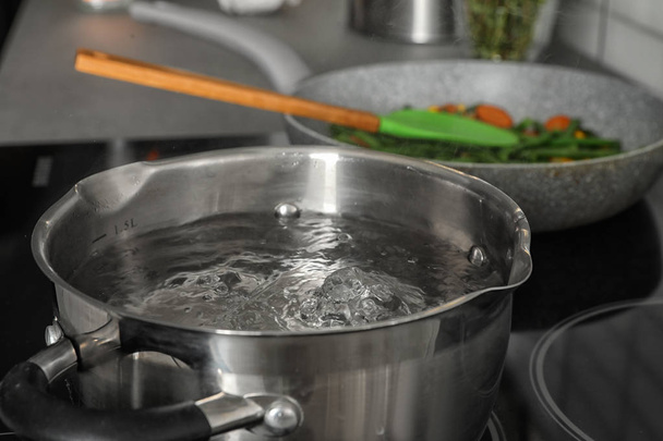 Pot with boiling water on electric stove in kitchen, closeup - Фото, изображение
