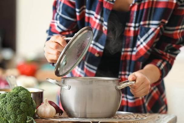 Mulher com panela de sopa quente saborosa na cozinha
 - Foto, Imagem