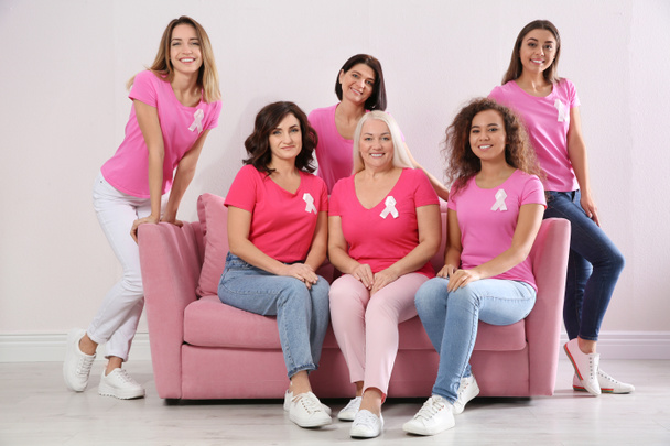 Group of women with silk ribbons on sofa near light wall. Breast cancer awareness concept - Foto, imagen