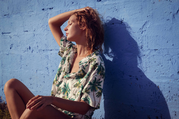 Kobieta w tropikalnej koszuli pozowanie przed niebieską ścianą - gorący letni dzień - Zdjęcie, obraz