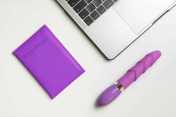 Concepto de viaje LGBT. Pasaporte púrpura, consolador y portátil en escritorio blanco. Buscando entradas en línea para citas
. - Foto, imagen