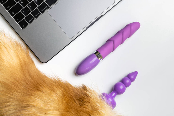 Dildo, anal plug tail and laptop on white desk. Online order or dating for casual sex, promiscuity and polygamy concept. - Photo, Image