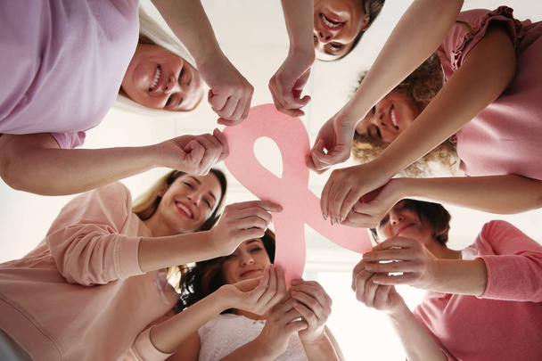 Group of women with silk ribbons on sofa near light wall. Breast cancer awareness concept - Foto, afbeelding