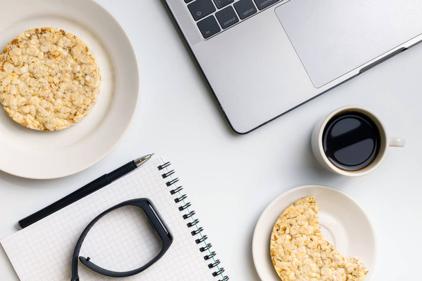 Healthy snacking at work during break time. Crispy rice rounds with coffee near the laptop and notebook. White organized desk. - Foto, Bild