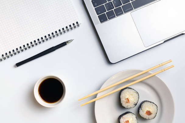 Sushi rolls snacking at work. Break time for sushi eating. Laptop and notebook on white organized desk. - Fotó, kép