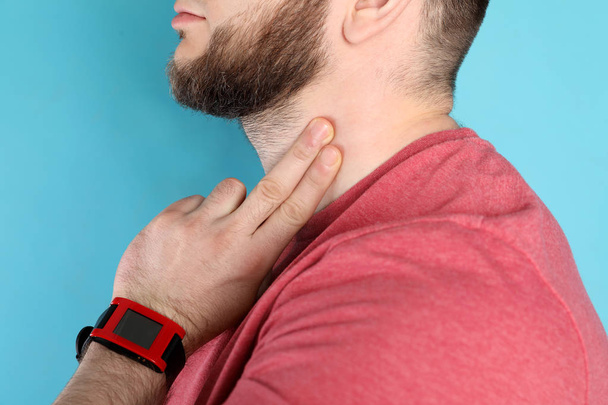 Young man checking pulse on neck against color background, closeup - Fotoğraf, Görsel