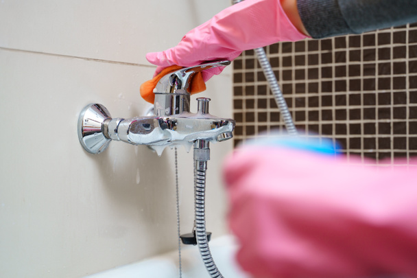 Женская рука в резиновых перчатках со смесителем для мытья ванн
 - Фото, изображение