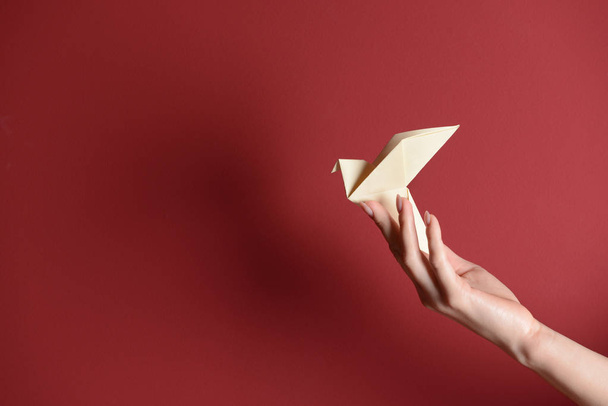 Female hand with origami bird on color background - Photo, Image
