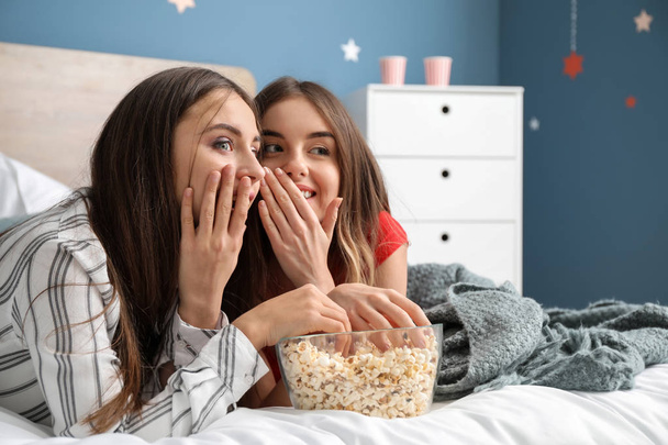 Молодые женщины смотрят телевизор и едят попкорн дома
 - Фото, изображение