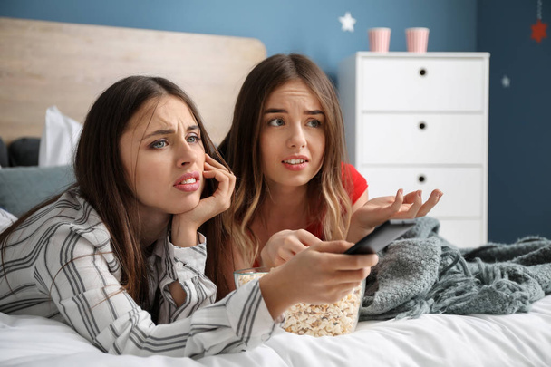 Запутавшиеся молодые женщины смотрят телевизор и едят попкорн дома
 - Фото, изображение