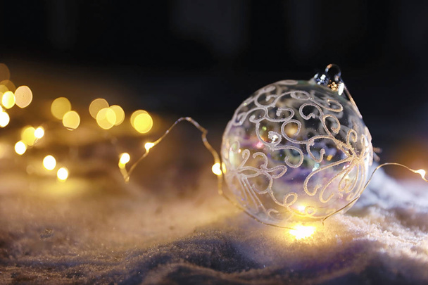 Christmas ball and fairy lights on white snow outdoors. Space for text - Valokuva, kuva