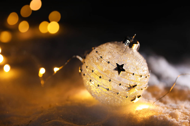 Bola de Natal e luzes de fadas na neve branca ao ar livre. Espaço para texto
 - Foto, Imagem