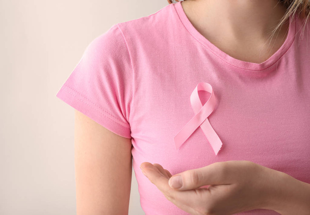 Woman with pink ribbon on light background, closeup. Breast cancer awareness concept - Foto, Imagen