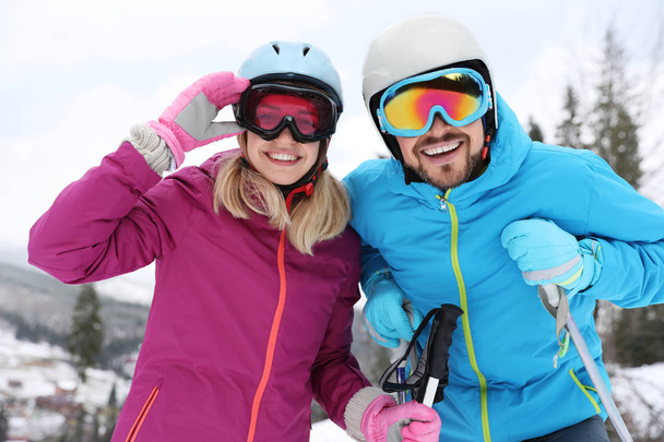 Happy couple with ski equipment sitting on snowy hill in mountains, space for text. Winter vacation - Zdjęcie, obraz
