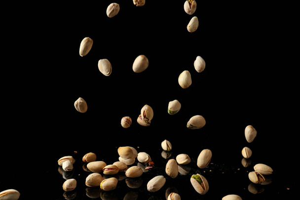 Falling pistachio nuts on dark background - Fotografie, Obrázek