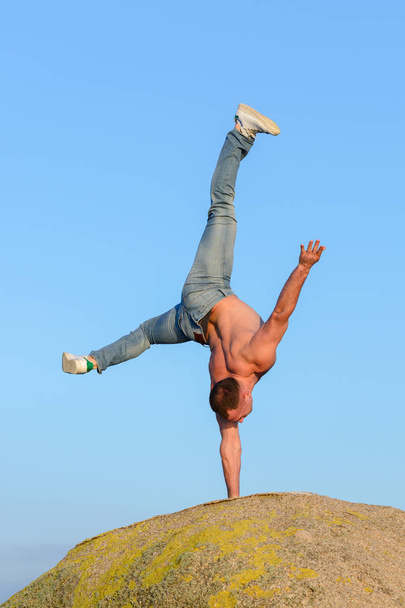 young man doing a handstand on a rock against a blue sky - Fotoğraf, Görsel